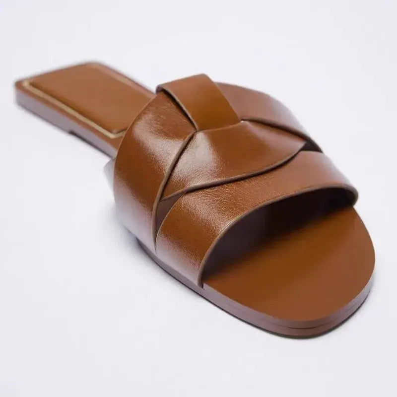 Brown leather cross-band slide sandal with open toe and flat sole, casual mule style.