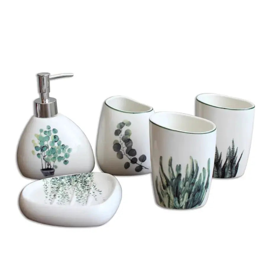 White ceramic bathroom accessory set by Simples Market with green plant prints; includes soap dispenser, lotion bottle, toothbrush holder, mouthwash cup and storage tray