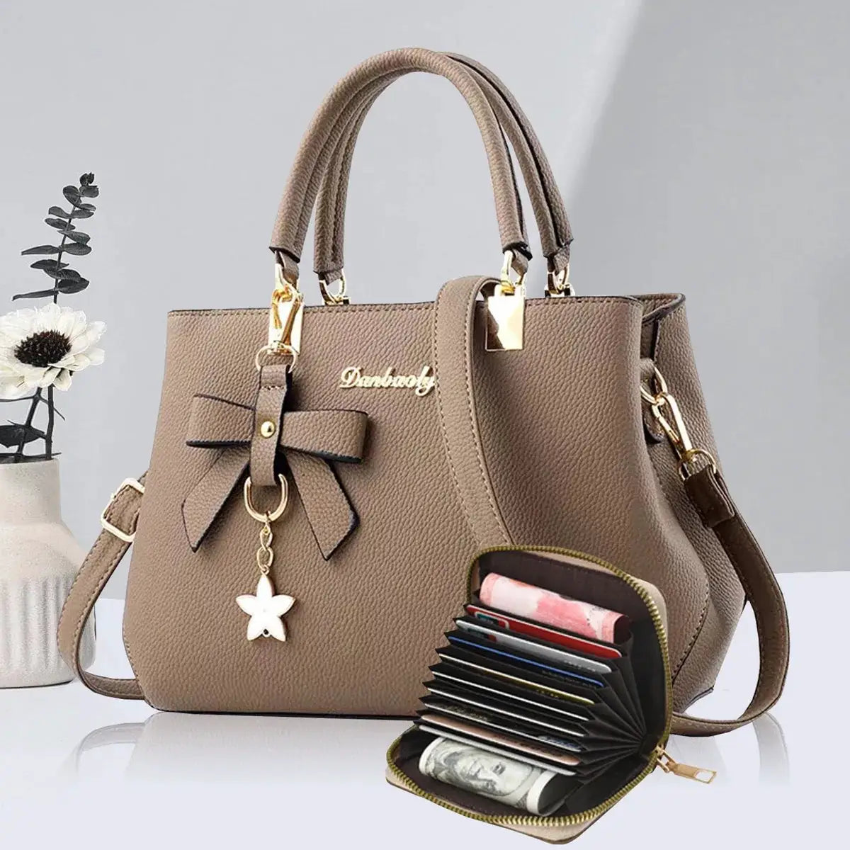 Bow-embellished taupe pebbled handbag by Simples Market with double top handles and gold hardware, paired with a compact wallet