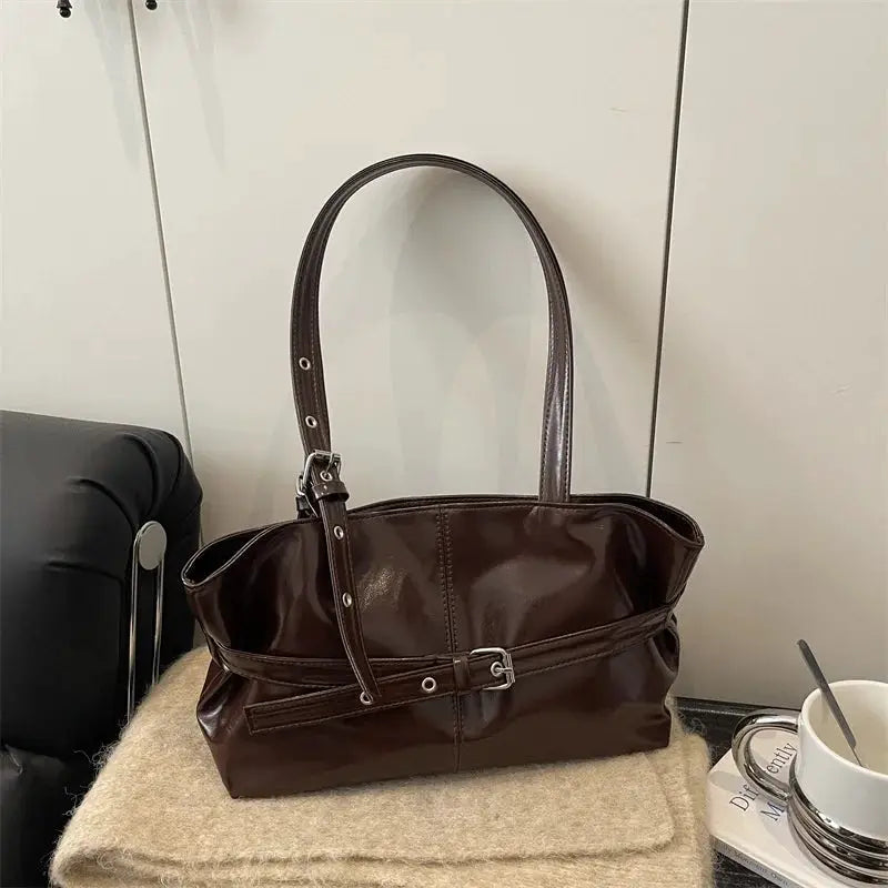 Brown leather handbag with belt-buckle strap, top handles, and adjustable shoulder strap by Simples Market