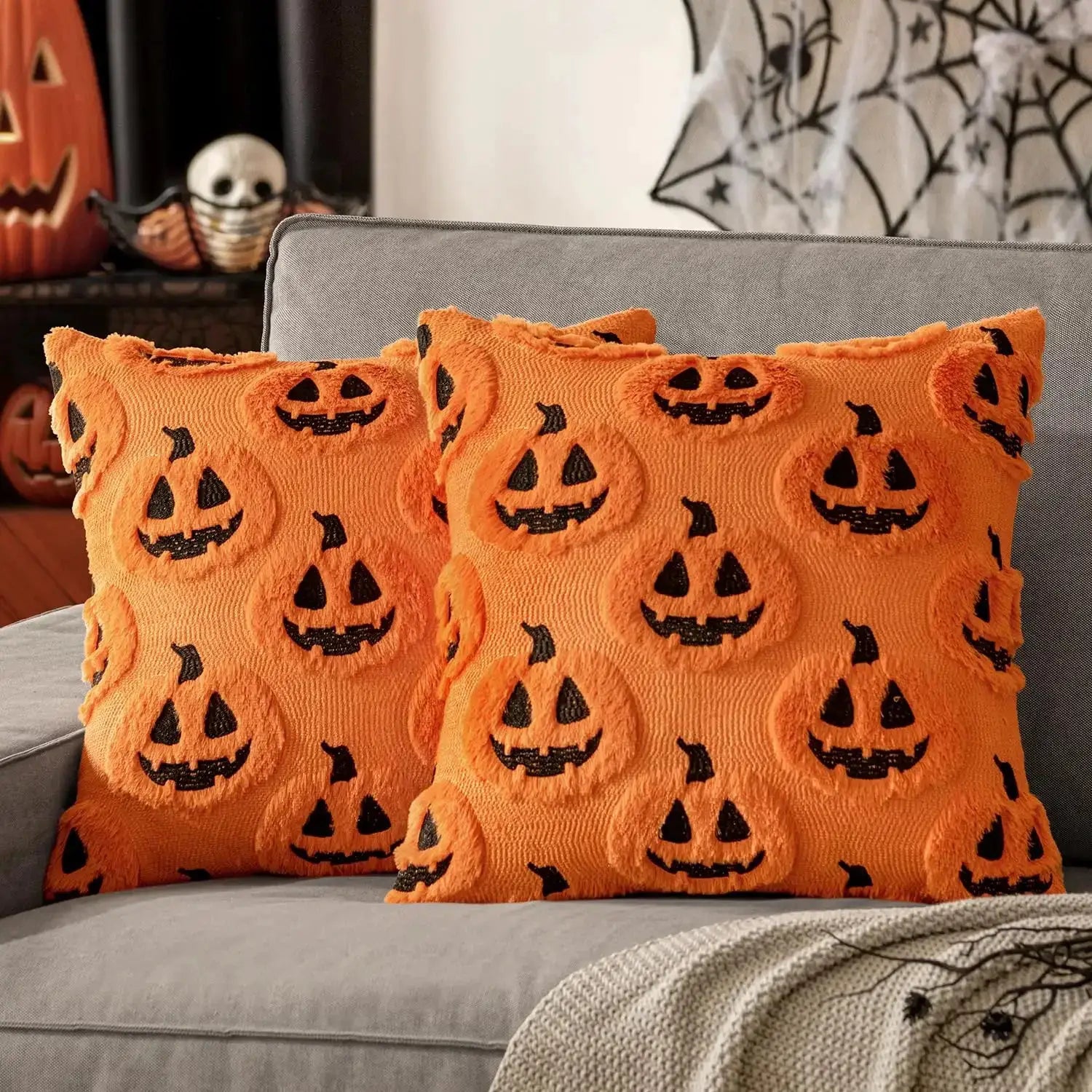 Halloween pumpkin-pattern plush pillow covers, orange with black jack-o’-lantern faces, pair on a gray sofa
