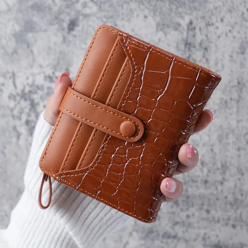 Mini crocodile-print clutch wallet with card slots and a wrist strap in tan-brown leather.