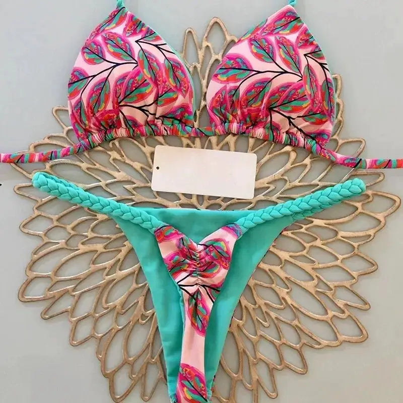 Women's bikini set with pink tropical print triangle top and turquoise braided-strap G-string bottom.