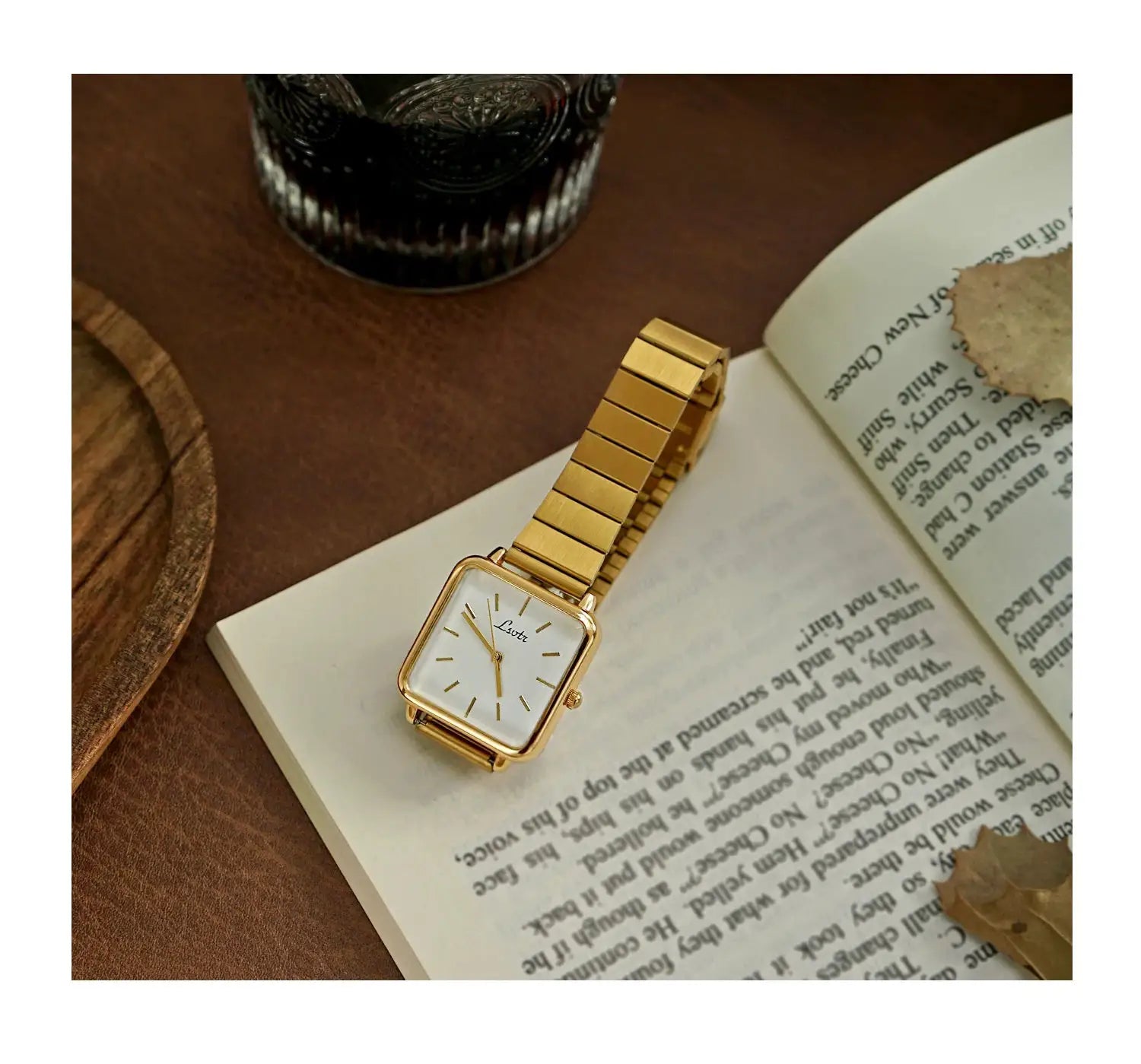 Gold-tone square-dial women's wristwatch with a stainless steel strap, on an open book.