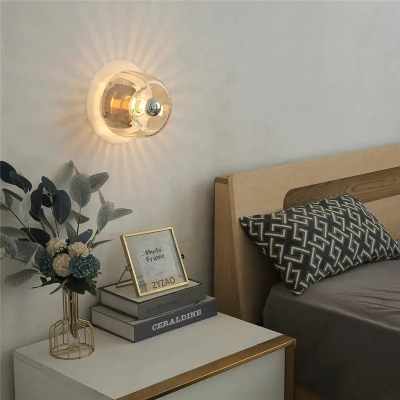 LED Bauhaus glass wall lamp with clear shade and warm brass finish on bedroom wall beside the nightstand.