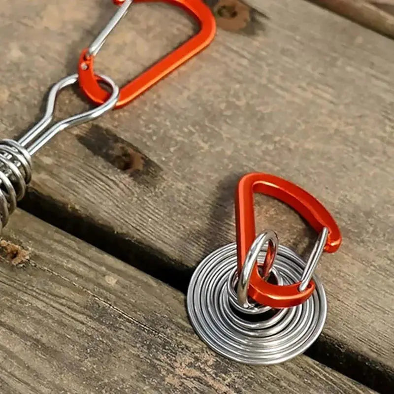 Rope buckle set for outdoor camping with orange carabiners and a coiled stainless steel spring on wood