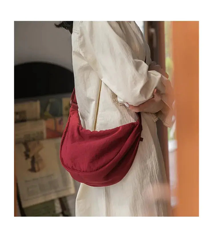 Red nylon padded crossbody bag with long shoulder strap, carried by a woman in a beige coat.