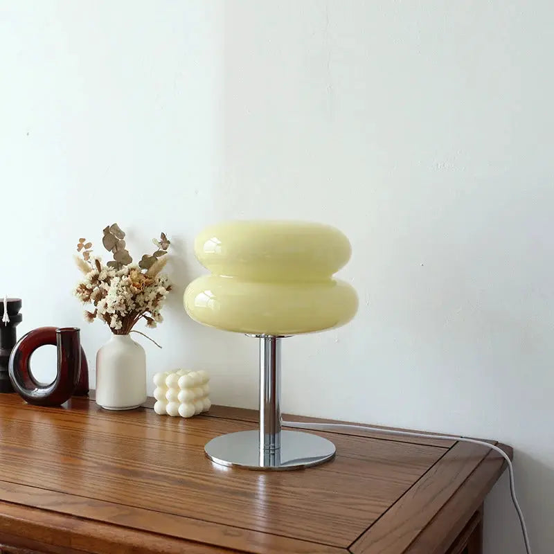 Macaron glass table lamp on chrome pedestal; pale yellow glass on a wooden table with 5 decor items