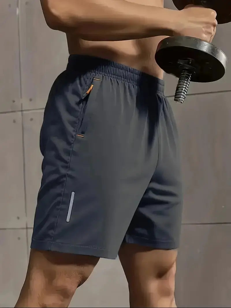 Men's gray athletic shorts with elastic waistband, orange zipper pulls on pockets, and a reflective leg stripe.