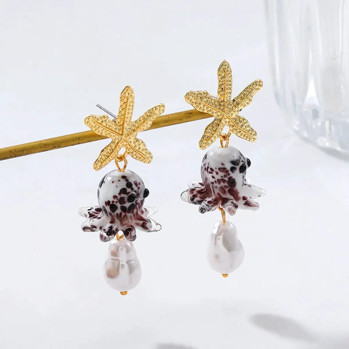 Two gold starfish drop earrings with white glass octopus charms and pearl drops
