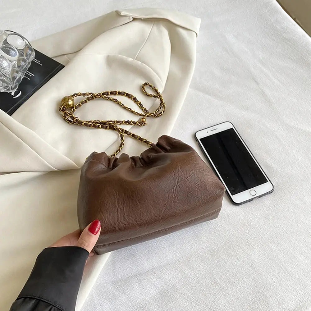 Simples Market women's brown leather crossbody bag with gold-tone chain strap and pleated hobo style.