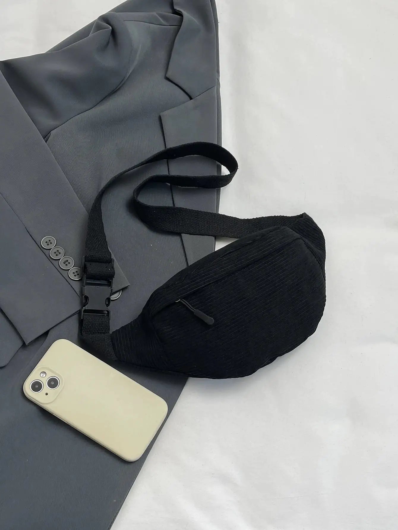 Black fanny pack waist bag with adjustable strap, shown on a gray blazer beside a smartphone