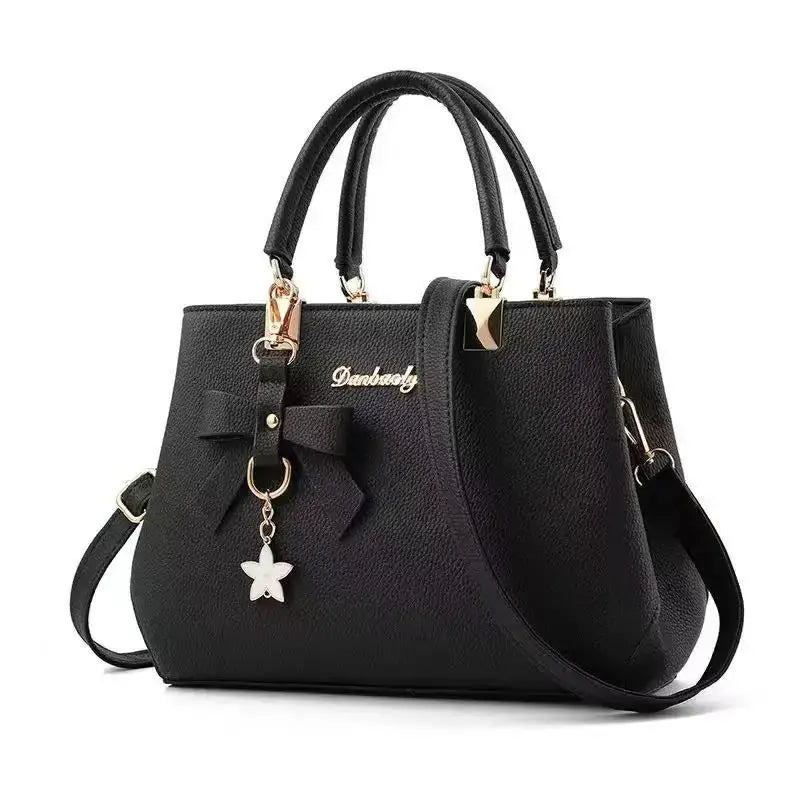 Black faux leather women's handbag with bow charm and star pendant, gold hardware, handles and detachable strap.
