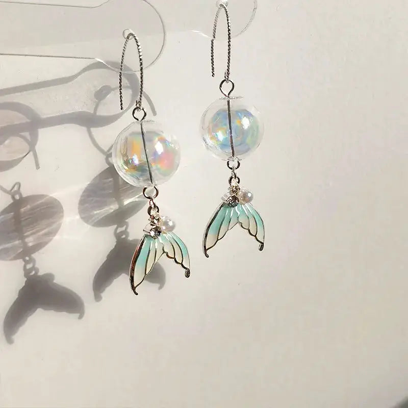 Pair of goldfish earrings by Simples Market with transparent iridescent bead and mint-green koi wing pendants.
