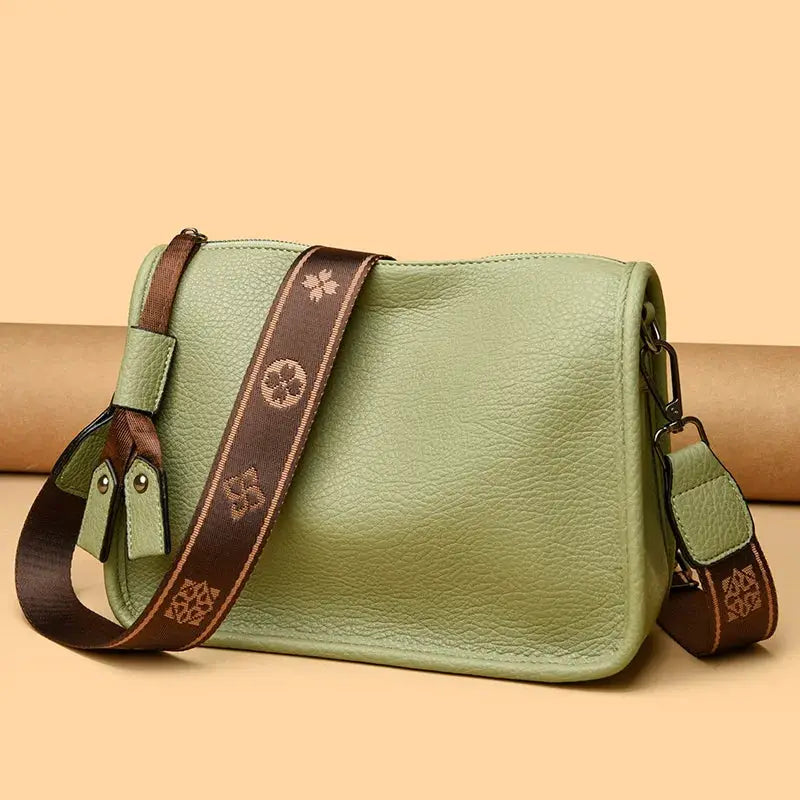 Leather tote bag in green for women with a soft pebbled texture, brown patterned crossbody strap and metal hardware.