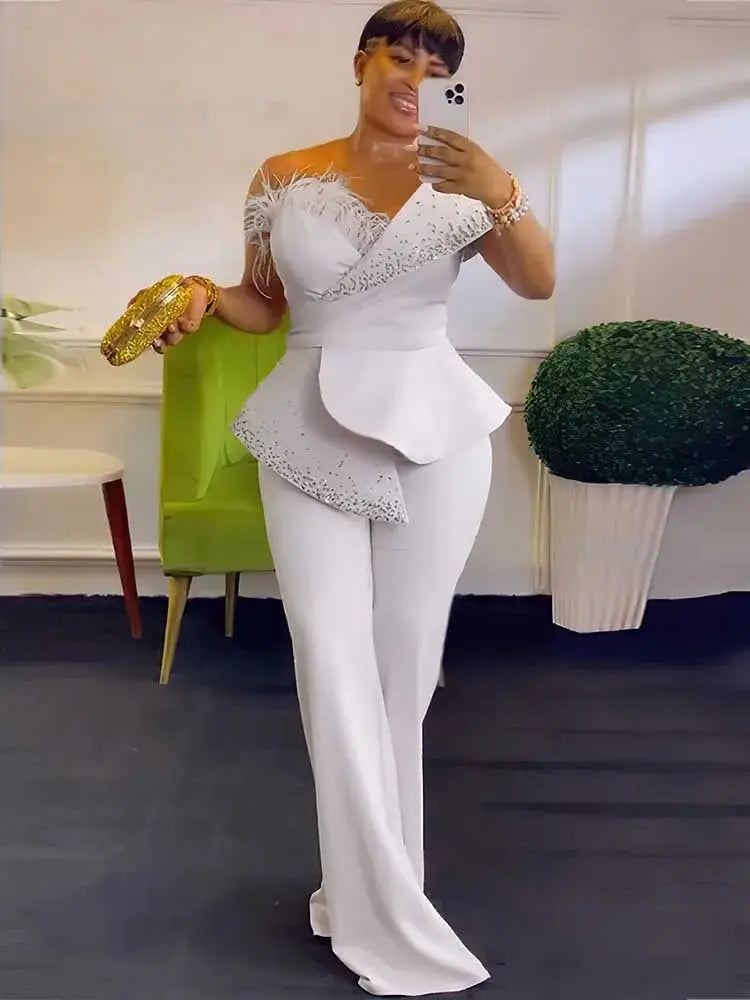 White strapless high-waist jumpsuit with asymmetrical peplum and rhinestone trim; wide-leg pants.