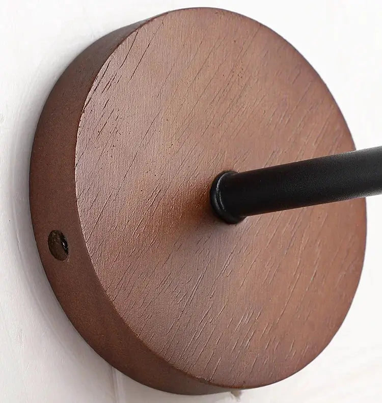 Wall sconce with round brown wooden backplate and black metal rod.