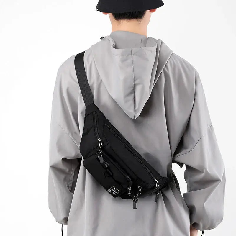 Men's black nylon waist bag by Simples Market with multiple zip pockets worn as a crossbody sling
