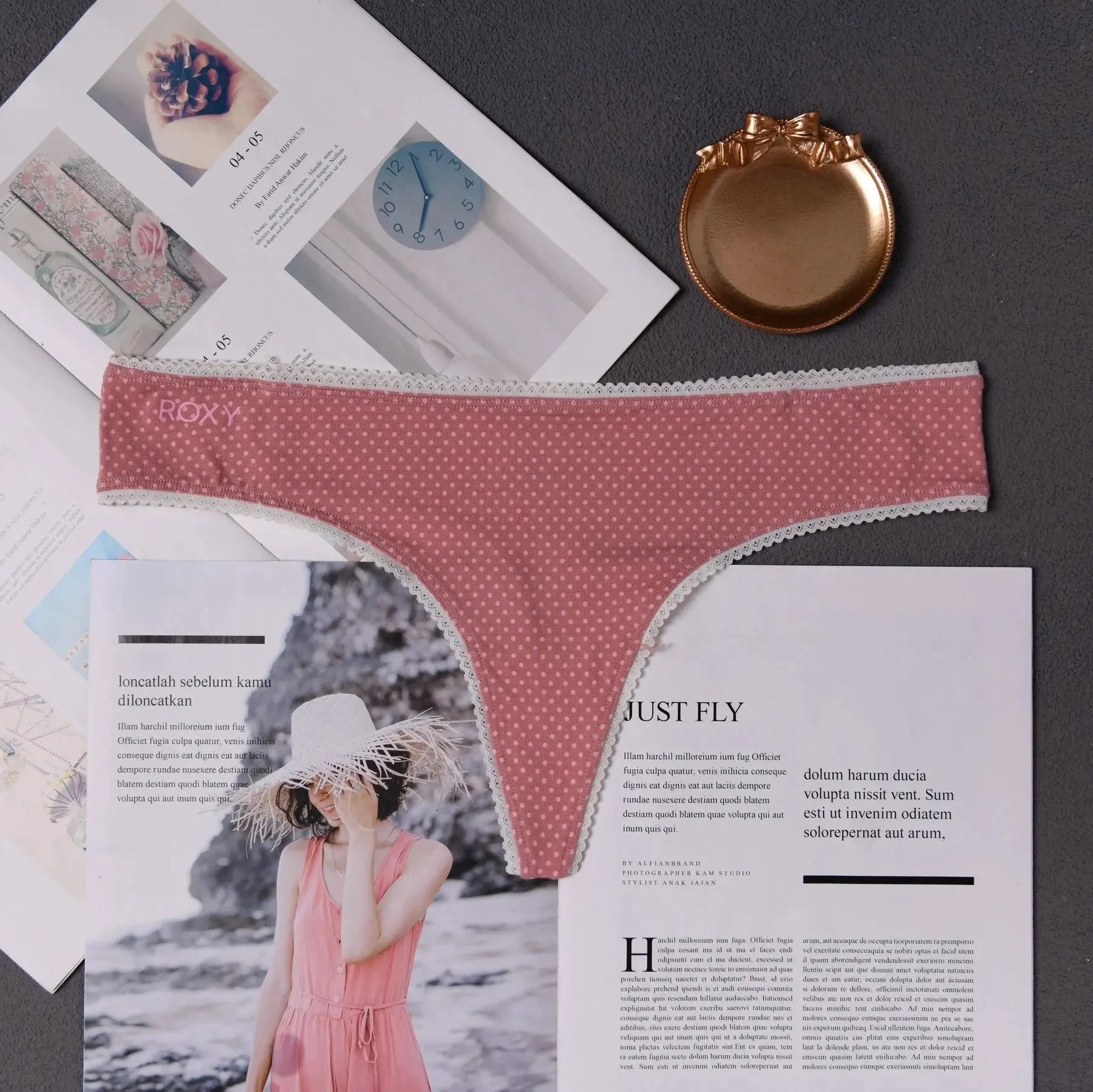 Women's pink polka-dot thong underwear with white lace trim; ROXY waistband, flat lay on magazines