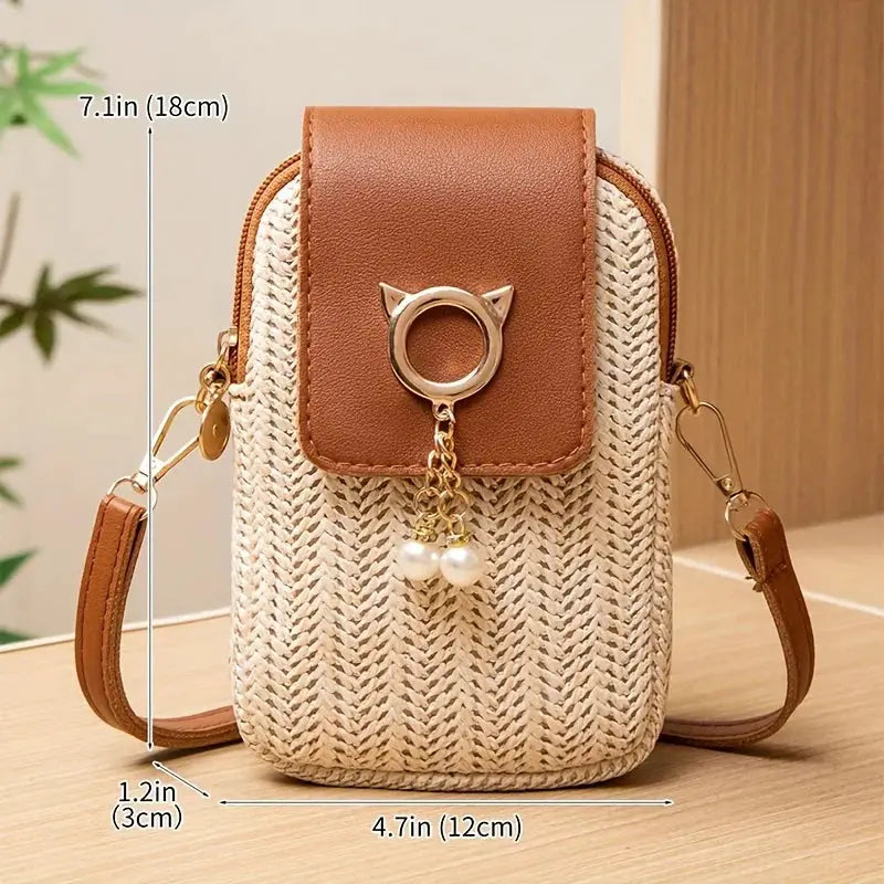 Mini crossbody phone bag by Simples Market; woven straw body with brown leather flap, gold ring accent, and pearl charms on a brown strap