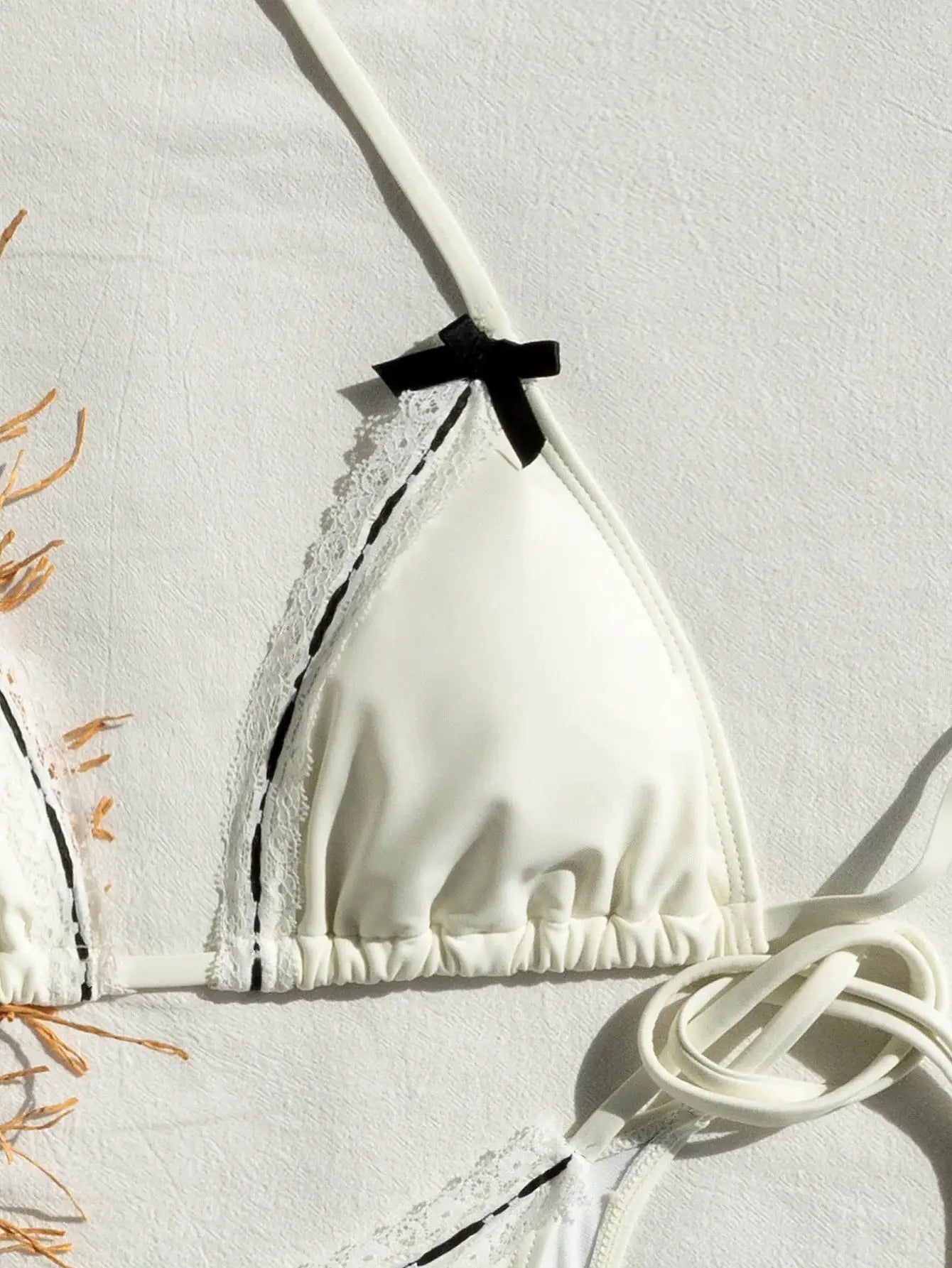 White triangle bikini top with lace trim and small black bow on the strap; tie sides.