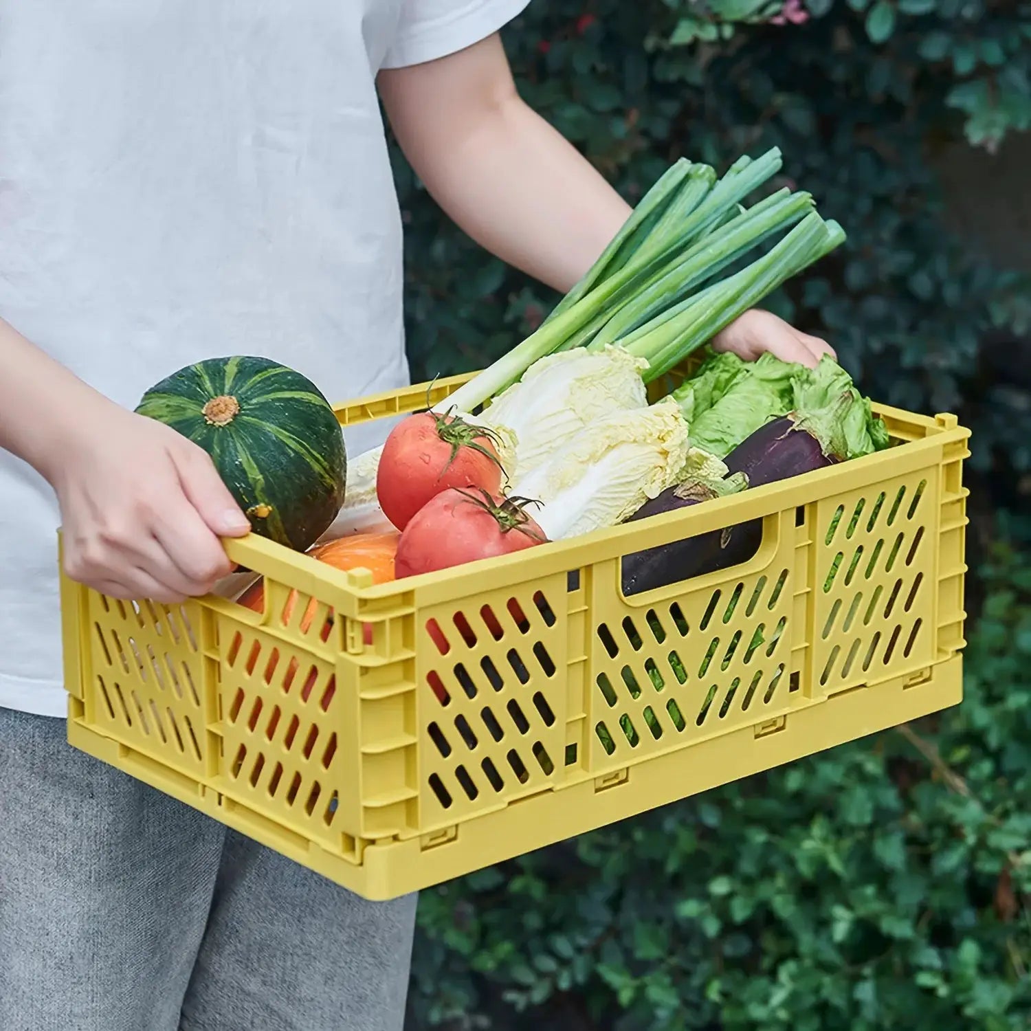Yellow plastic foldable storage crate, portable and stackable, filled with fresh vegetables.