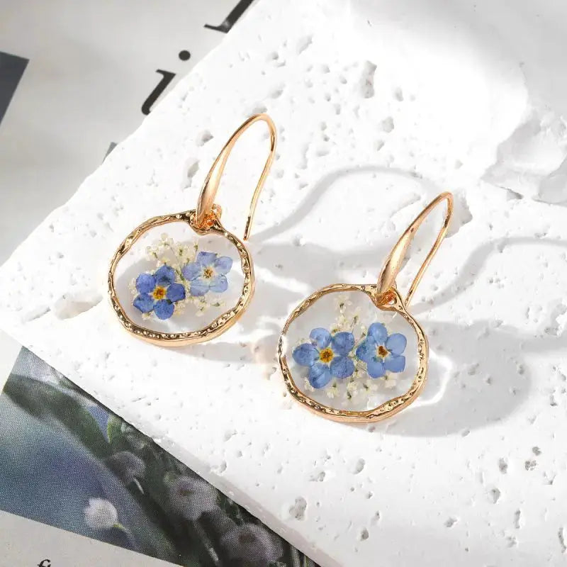 Natural flower dangle earrings, pair featuring blue pressed flowers in epoxy resin in gold-tone frames
