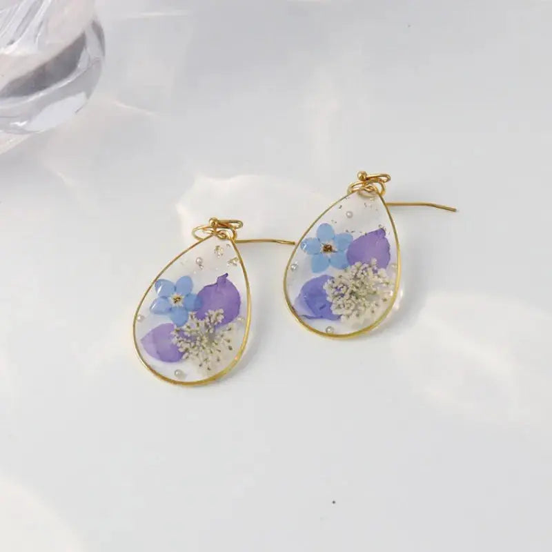 Simples Market pressed flower earrings—teardrop epoxy resin with blue and purple flowers in a gold-tone bezel, pair.