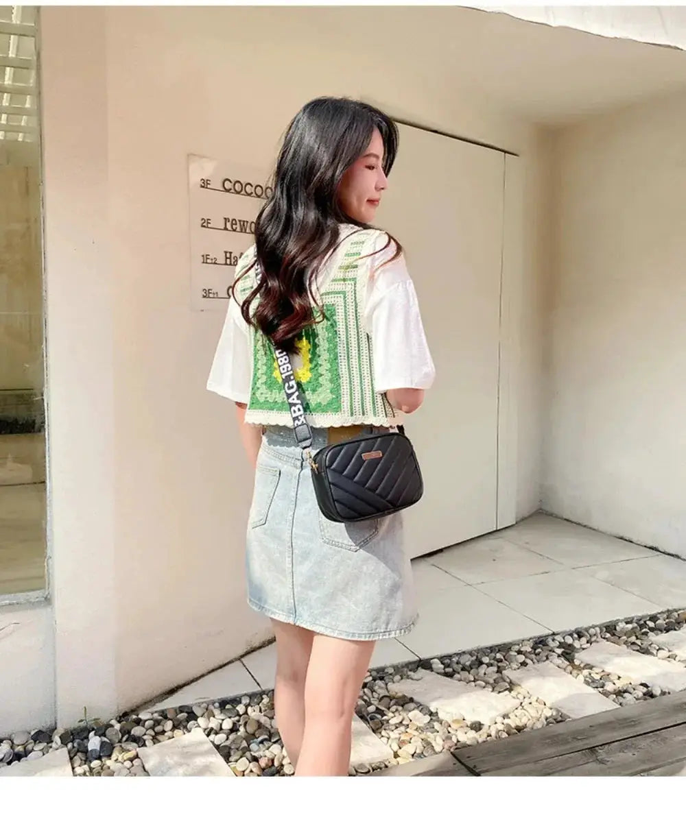 Shoulder bag black quilted PU crossbody with striped strap, worn with white top and denim skirt.
