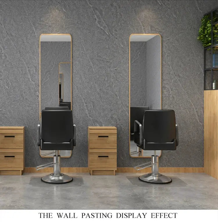 Hair salon station with two black styling chairs, tall mirrors, and wooden cabinets against a gray textured wall.