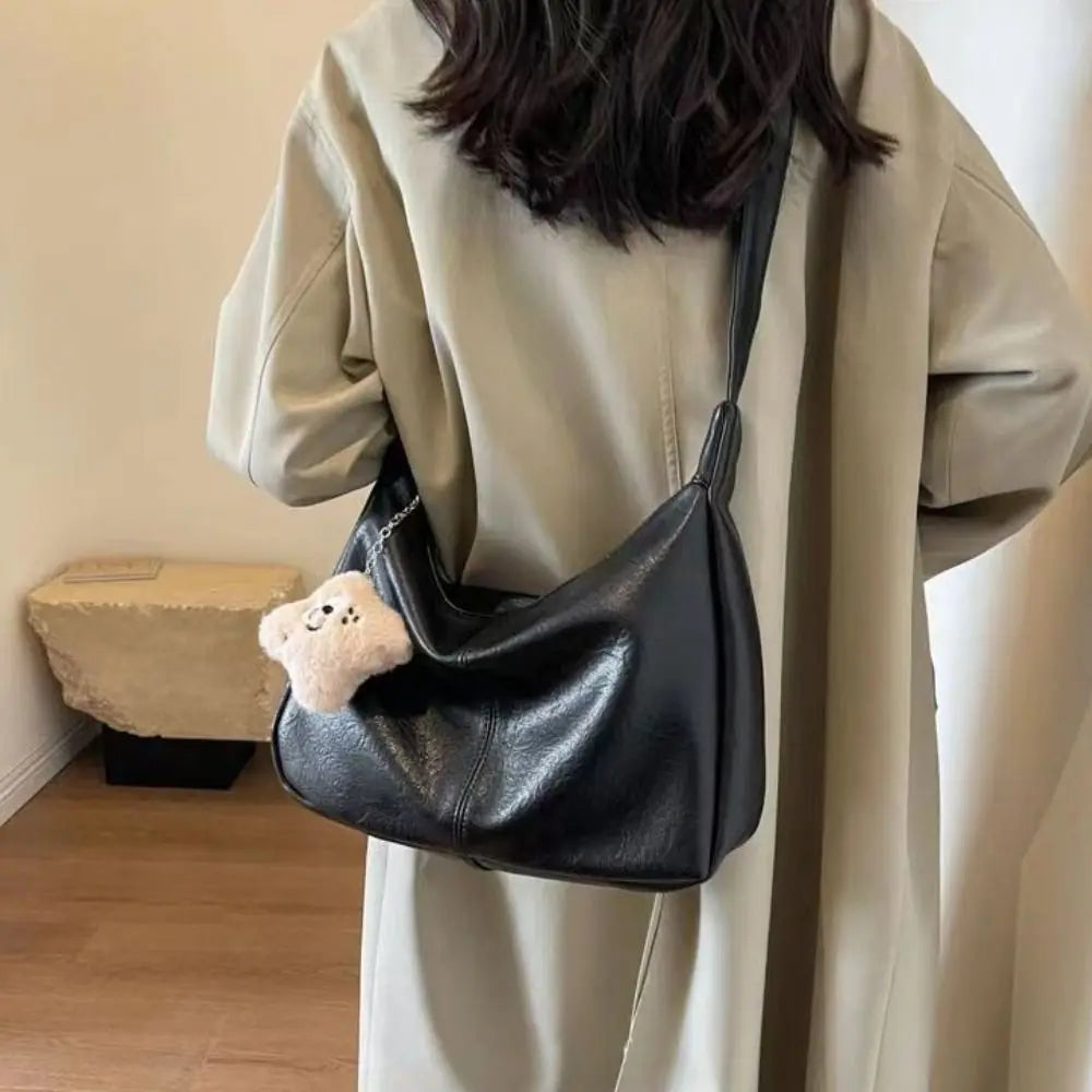 Trendy black PU leather slouchy shoulder bag, large-capacity with long strap and cream teddy keychain.