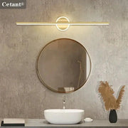 Modern LED wall lamp by Cetant, gold finish long strip with circular accent above round bathroom mirror