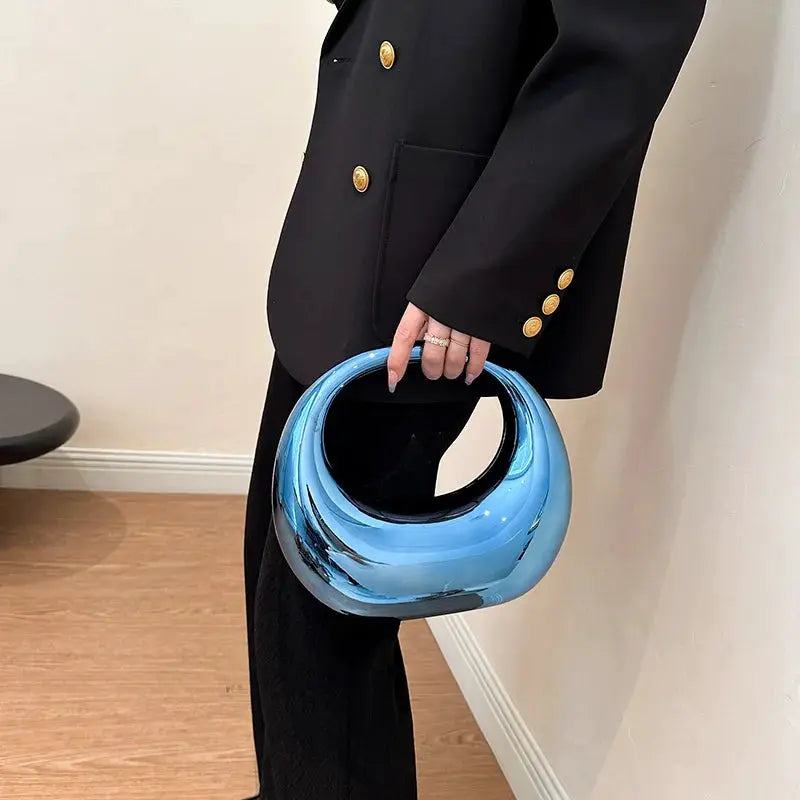 Blue metallic round-handle PVC handbag carried by a woman in a black suit with gold buttons.