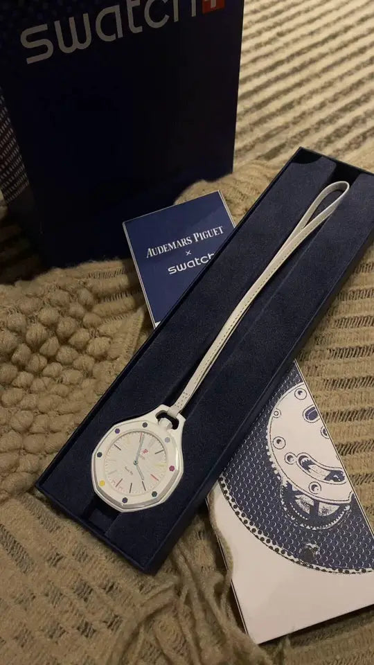 White Swatch quartz watch with colorful dial accents in navy presentation box; Audemars Piguet x Swatch card included.