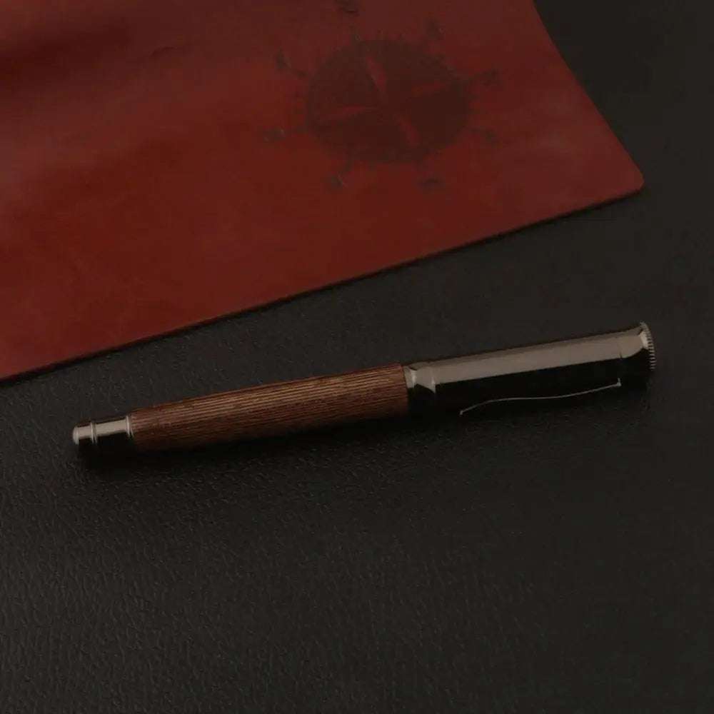 Simples Market wooden fountain pen with tiger-skin pattern and gun-grey cap on a black surface beside a red notebook.