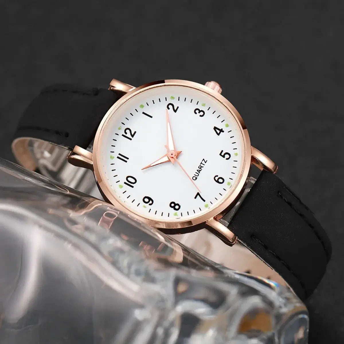 Women's rose gold-tone quartz wristwatch with white dial, black Arabic numerals, and black leather strap.
