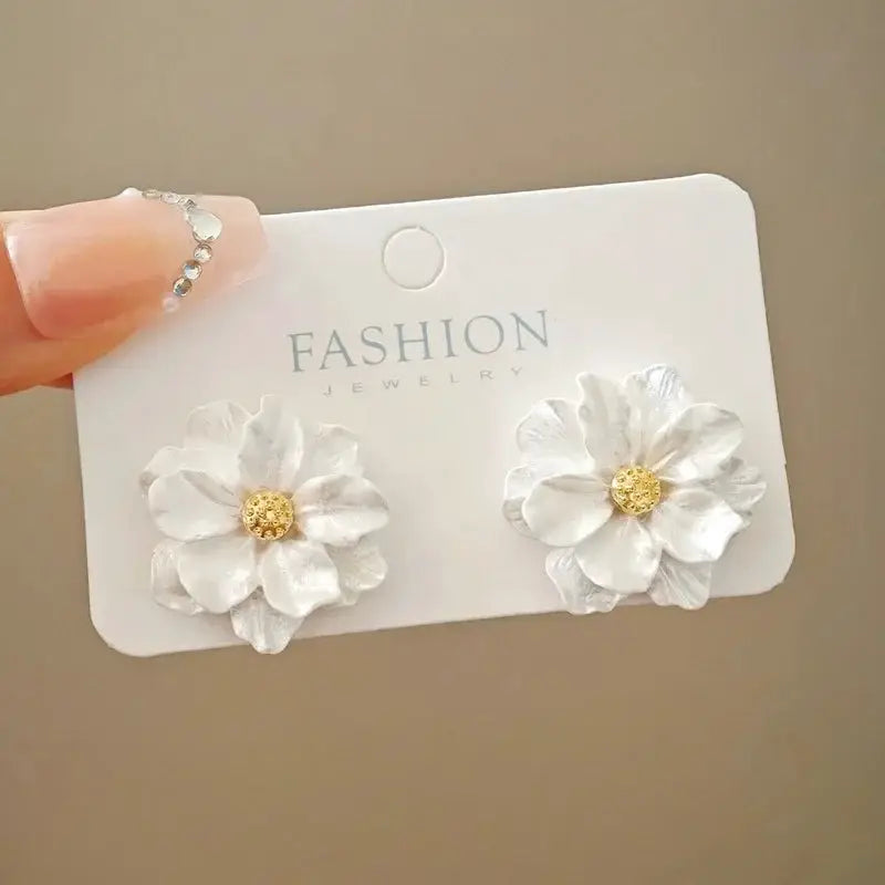 Pair of white enamel flower earrings with gold centers on a fashion jewelry card