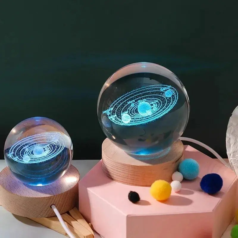 Two 3D crystal ball night lights with laser-engraved solar system designs, blue glow on wooden bases
