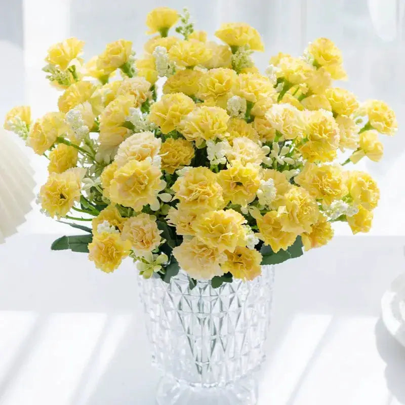 Artificial yellow carnation bouquet with white filler flowers in a clear faceted glass vase
