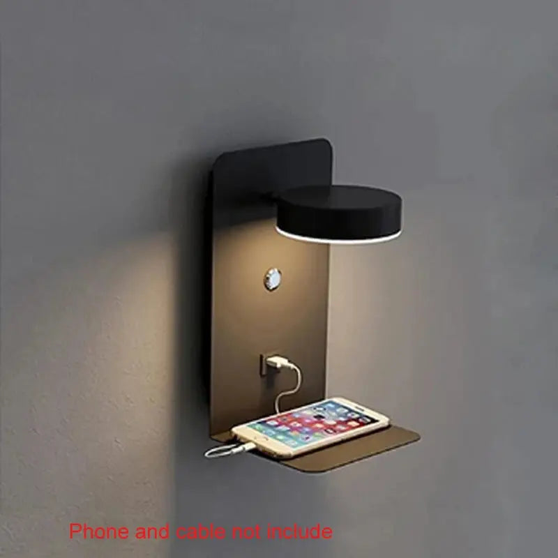 Bedroom LED wall lamp with USB charging, bronze backplate and black circular shade, small shelf holds a phone