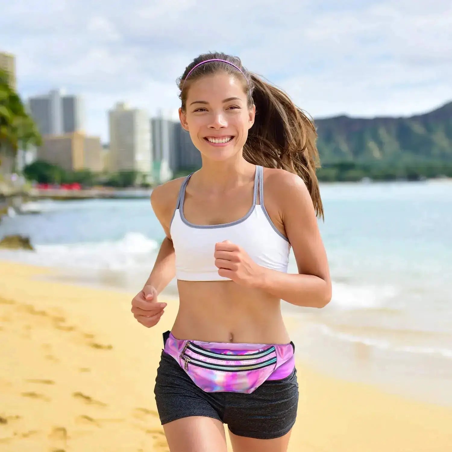 Waist bag holographic fanny pack with rainbow laser shine, worn at the waist by a woman jogging on a sunny beach