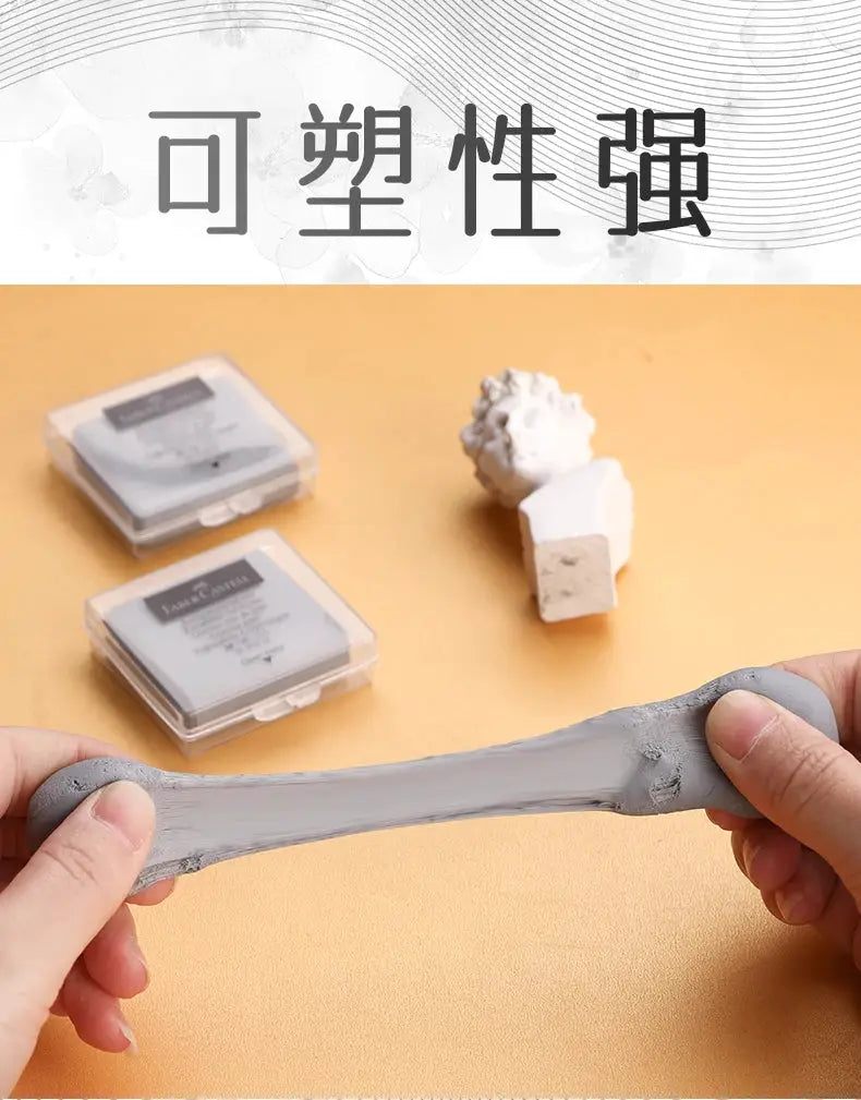 Faber-Castell kneaded eraser, gray, stretched by hands; two boxed erasers visible in background.