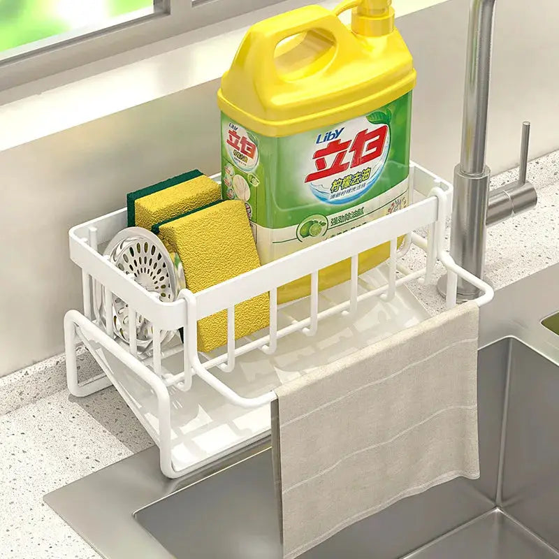 White kitchen sink drain rack with Liby dish soap bottle, two yellow/green sponges, and towel.