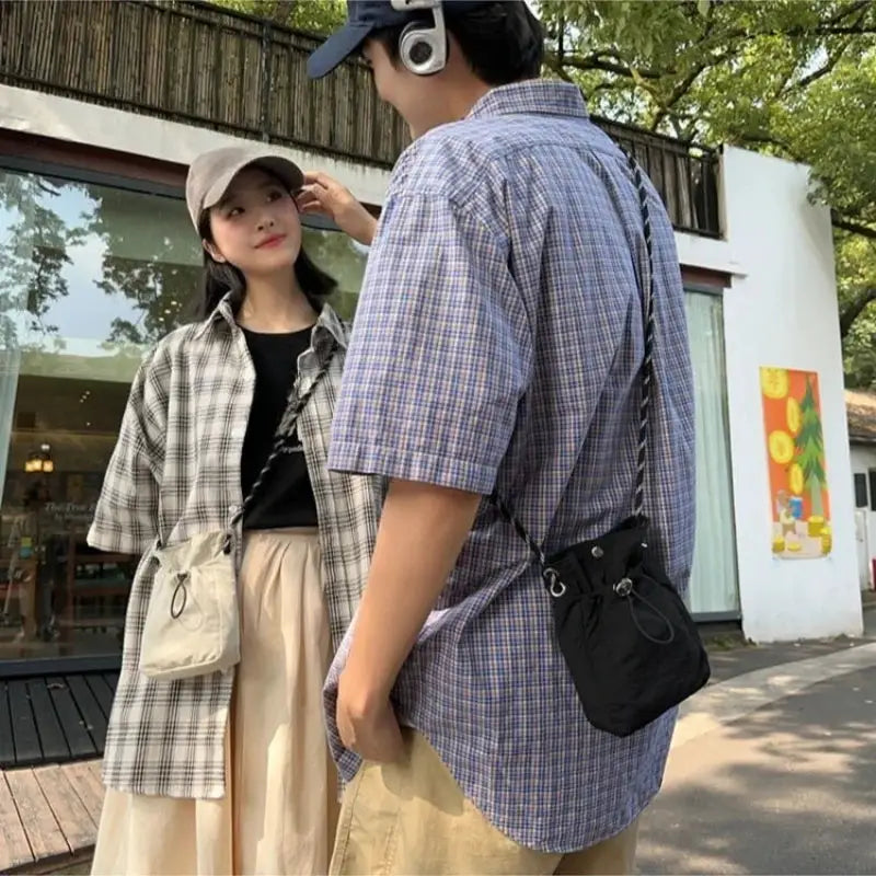 Nylon crossbody bags: black compact square bag and beige canvas mini purse worn by a couple.