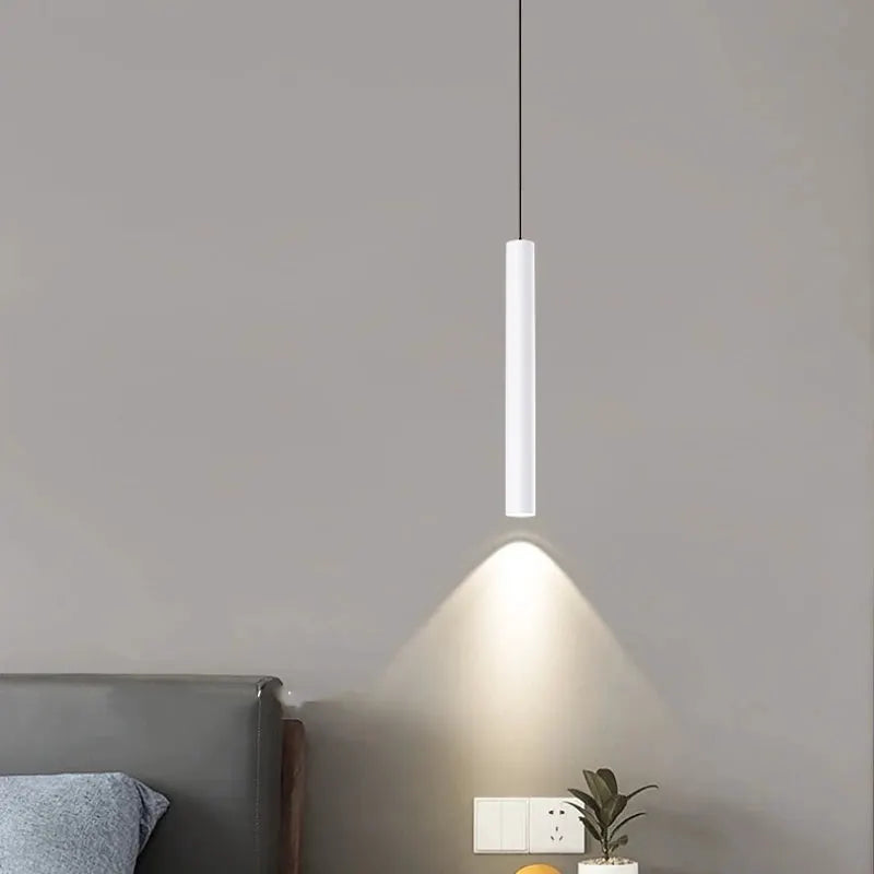 Minimalist bedside pendant lamp, white cylindrical LED, hanging from a black cord above the bed.