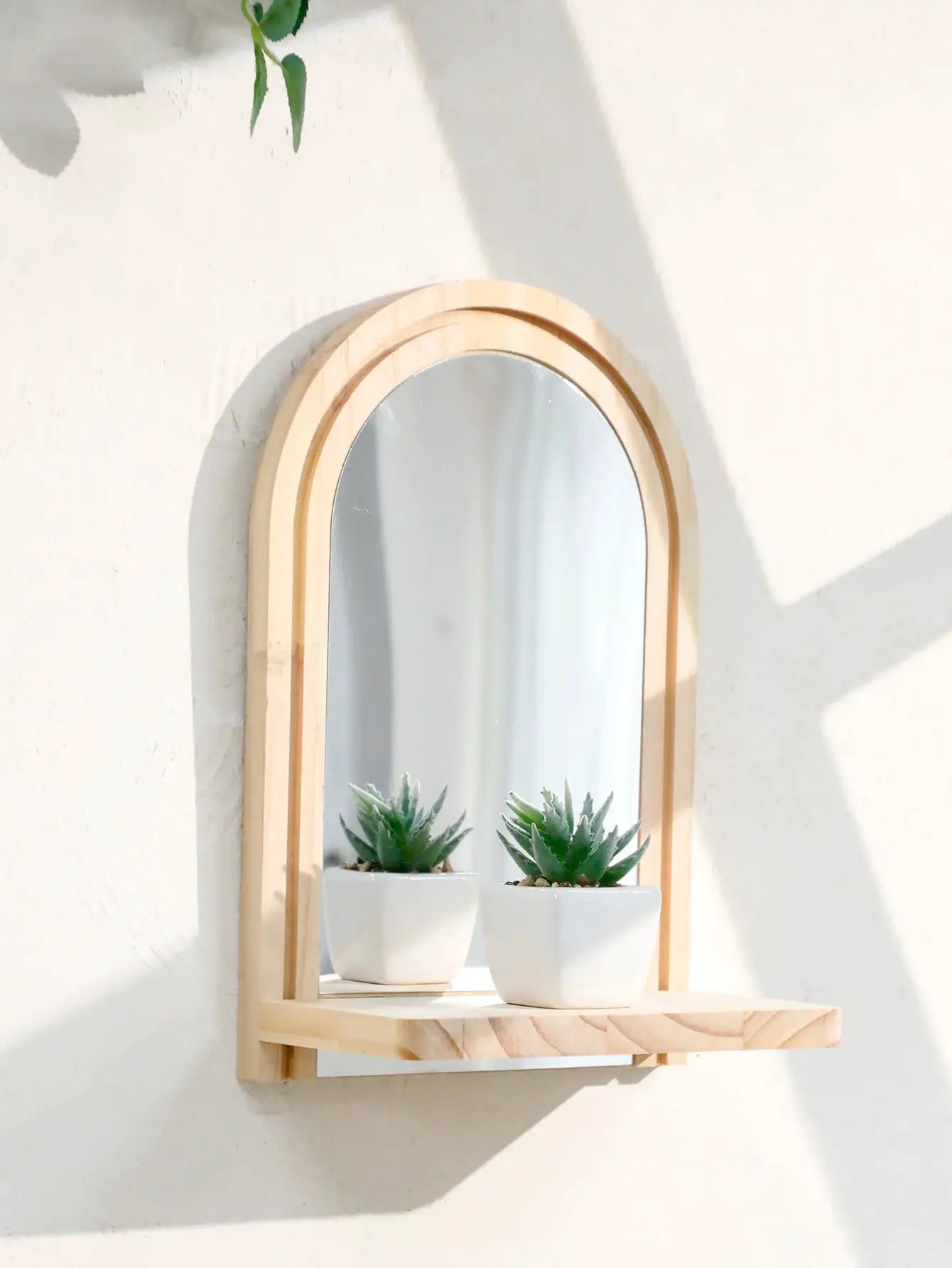 Boho-style wooden arch wall shelf in natural finish with a mirror center and two white pots with succulents