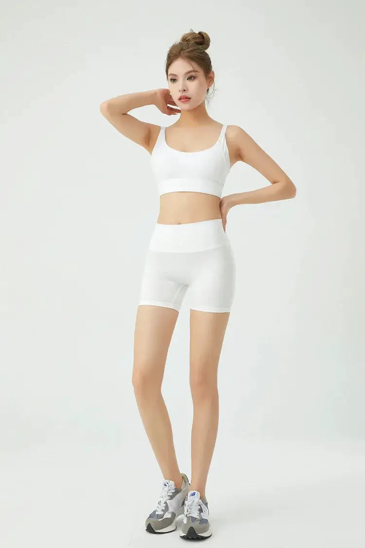 White athletic two-piece set with sports bra and shorts; model in gym wear.