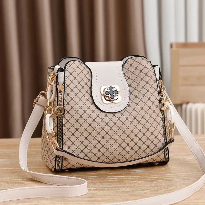 Simples Market women's bucket crossbody handbag with beige check print, gold hardware and floral emblem.