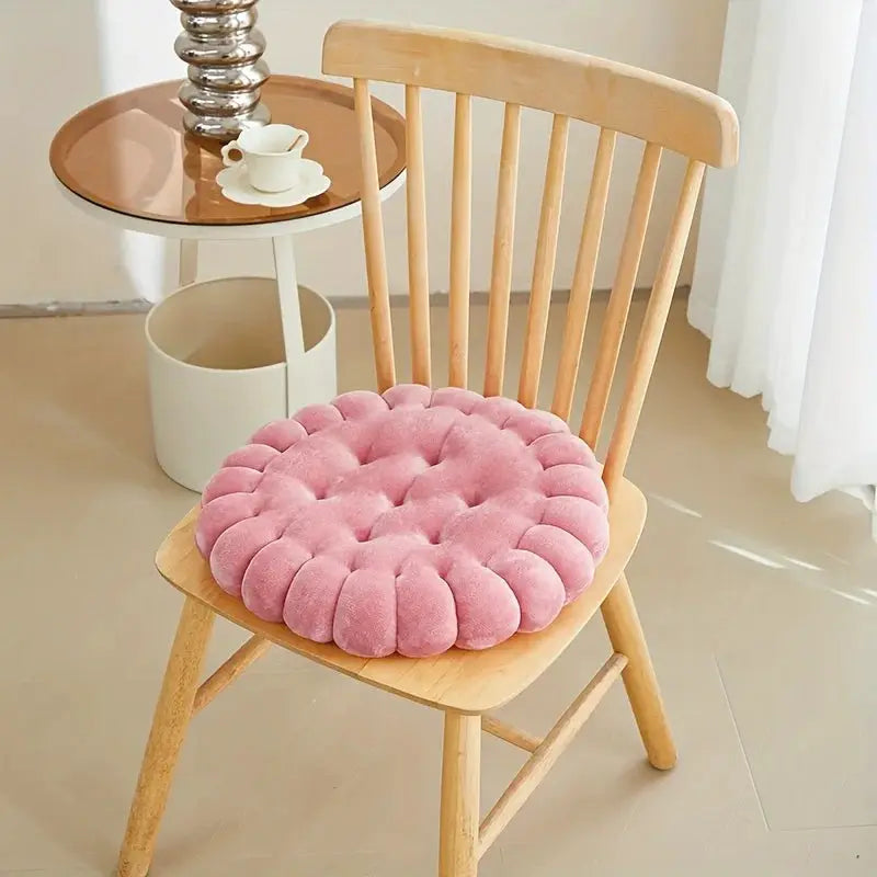 Large pink biscuit-shaped plush cushion on a wooden chair seat