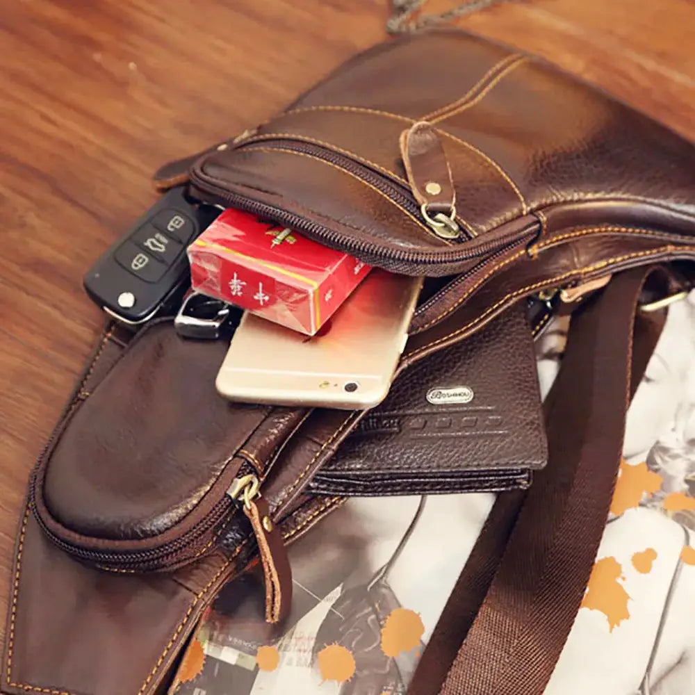Men's brown genuine leather crossbody sling bag by Simples Market with multiple pockets and visible items.
